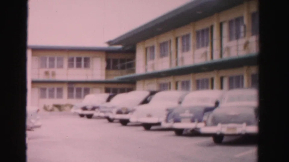 Wide view of parked 1950s cars along a two-story Dade County motel with green awning and exterior corridors.