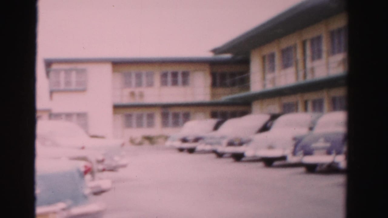 1955 Dade County, Florida home-movie frame showing classic cars parked outside a two-story tropical lodging building.