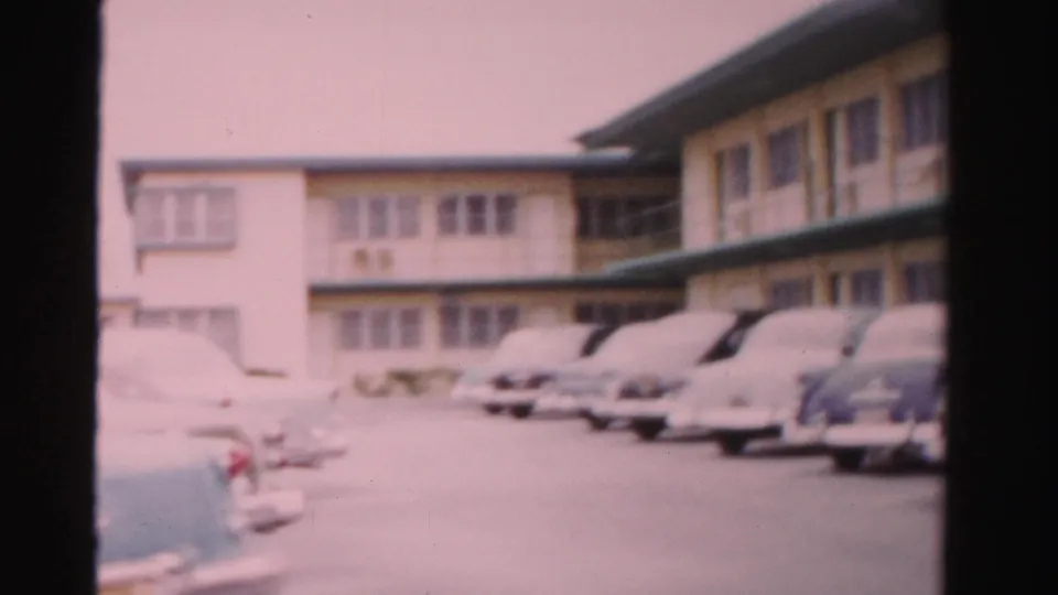 1955 Dade County, Florida home-movie frame showing classic cars parked outside a two-story tropical lodging building.
