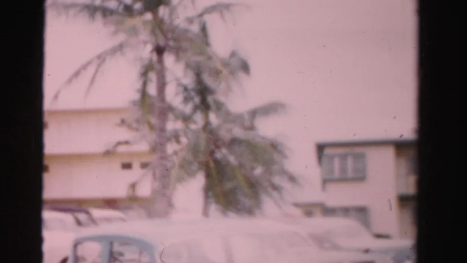 1955 Dade County frame showing a blue classic car in the foreground with palm trees and lodging exterior behind.