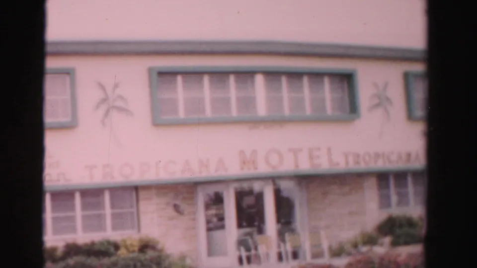 1955 Dade County view of the Tropicana Motel front with green-trimmed windows, pale facade, palm decals, and entrance doors.