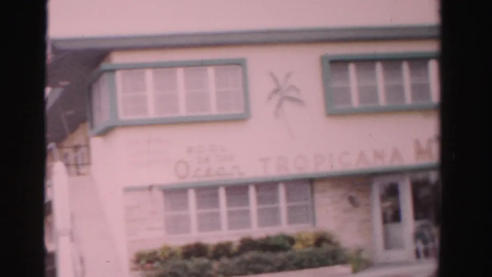 Dade County Tropicana Motel exterior showing the sign band, green-trimmed windows, planted shrubs, and a side doorway.