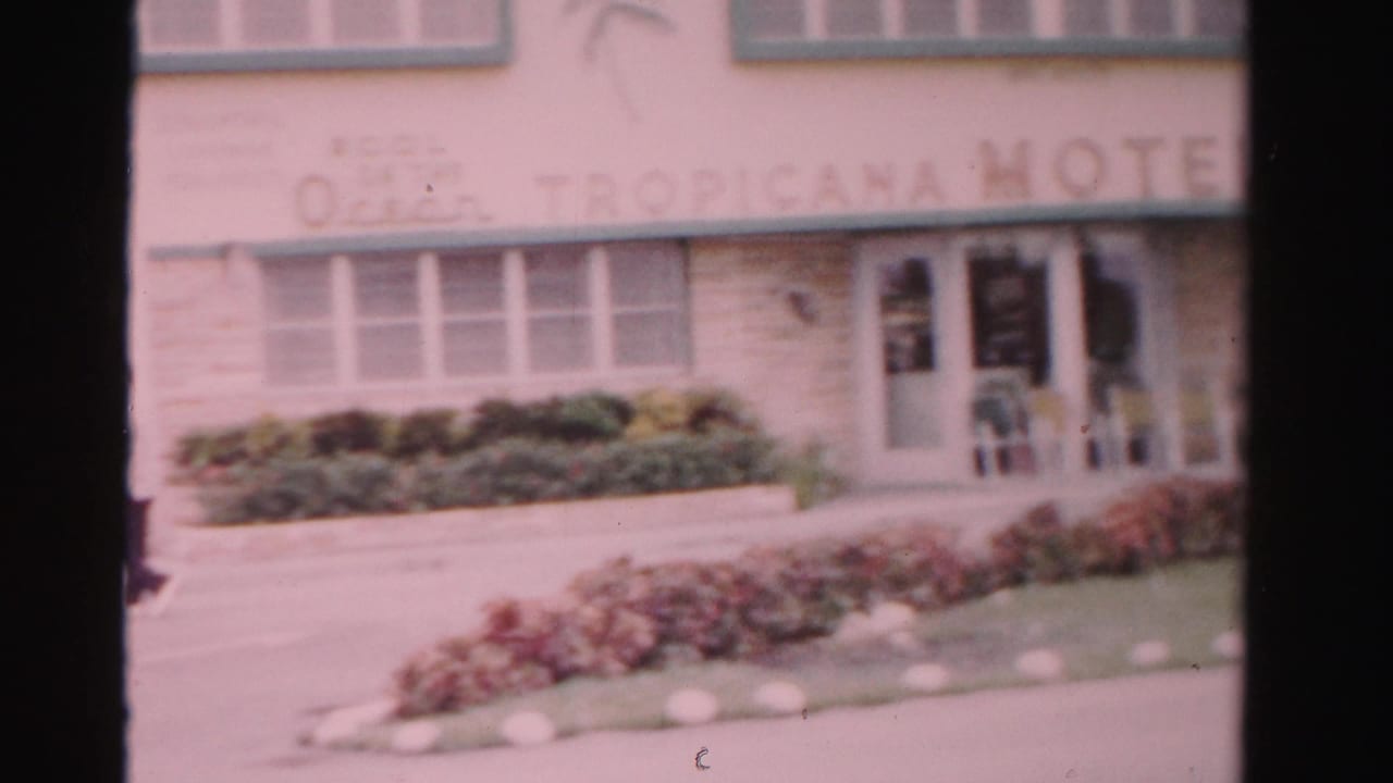 Motel entrance with faded Ocean Tropicana Hotel lettering, windows and low landscaping.