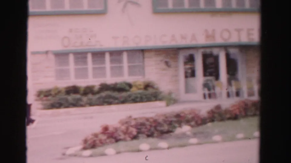 1955 Dade County street view of the Ocean Tropicana Hotel sign, entrance doors, low shrubs and flower beds along the motel facade.