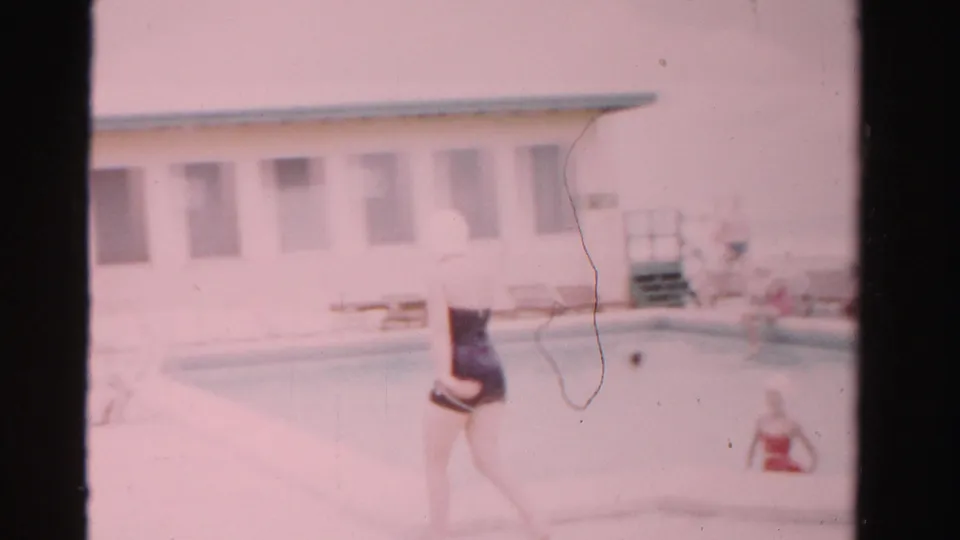 At the pool in Dade County, Florida, the woman walks near the water while a low poolside building and another swimmer are visible.
