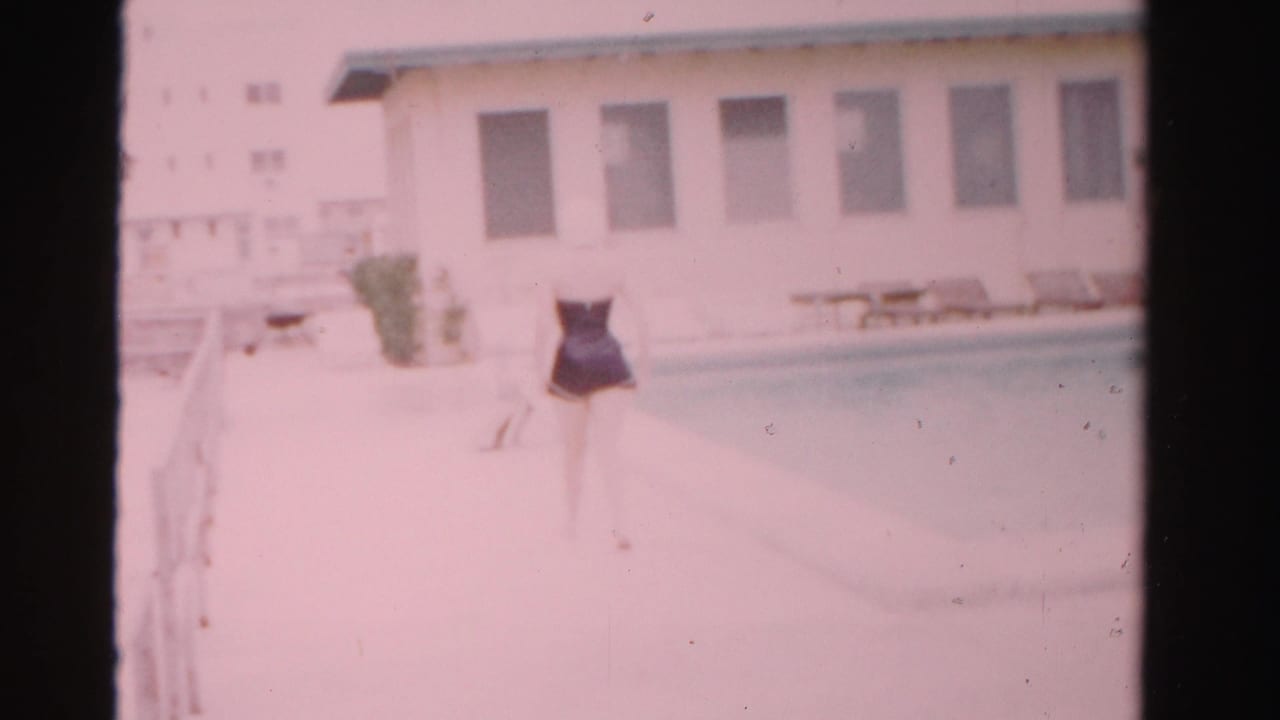 Woman continues along the poolside walkway with the building and lounge chairs in the background.