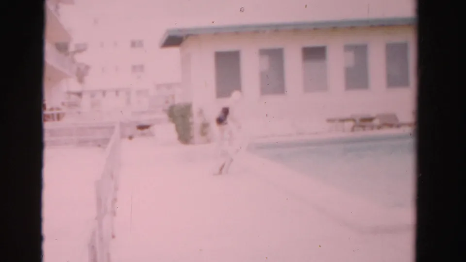 Soft 8mm frame from Dade County in 1955 showing a woman at the pool edge, with windows, railings, and deck furniture behind her.