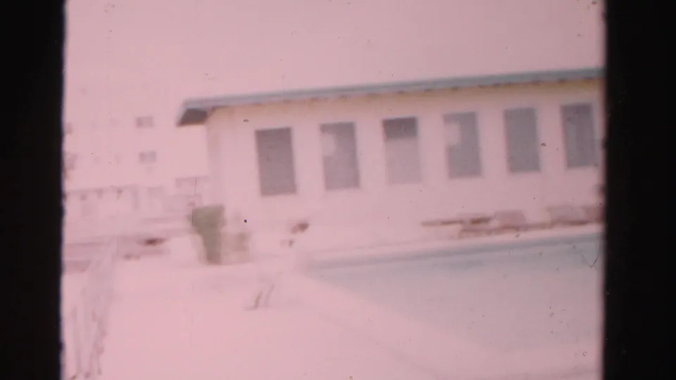 Final 1955 Dade County frame showing the woman low near the pool edge or entering the water, with the pool and white building visible.