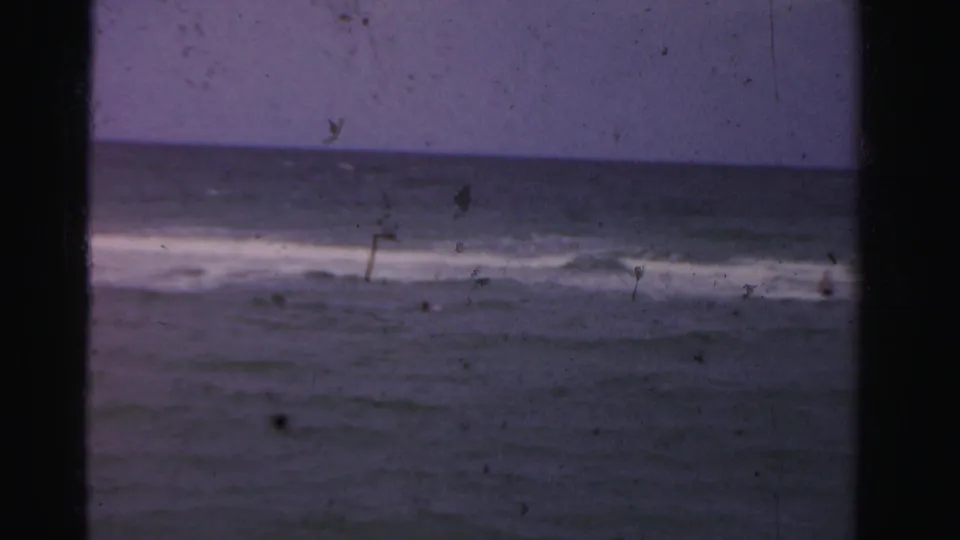 1955 Dade County ocean view with a level horizon, breaking waves, faded blue-purple color, and small swimmers visible in the water.