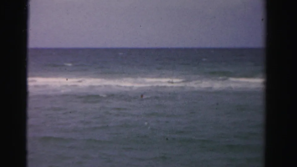 1955 Dade County 8mm view of low ocean waves and muted sky seen through a dark foreground frame.