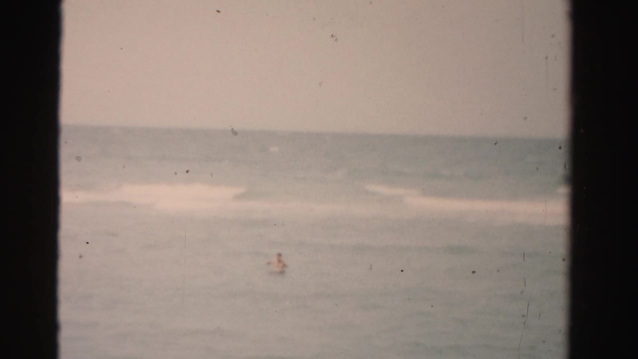 Small swimmer figure in open water beneath a hazy sky.