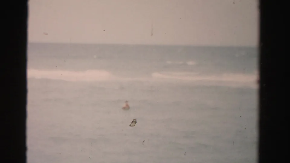 A lone swimmer remains distant in calm Florida ocean water, with faded film color and visible dust.