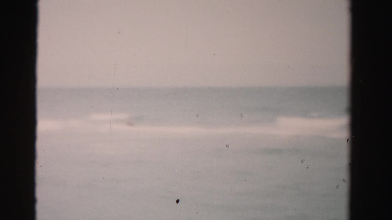 Distant ocean waves under a pale sky with dark 8mm frame borders.