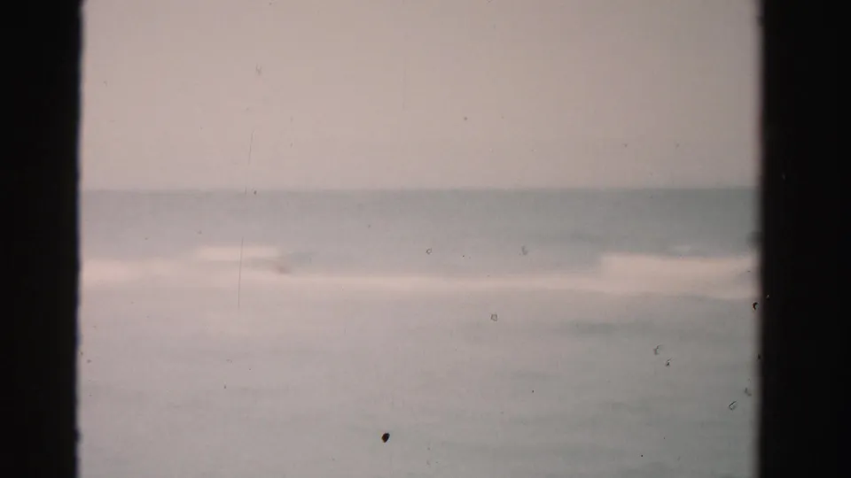 1955 Dade County 8mm frame showing soft ocean waves and a faint horizon, with the swimmer barely visible or out of view.