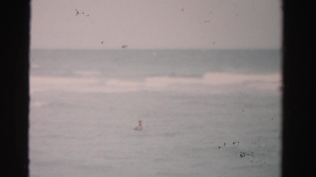 Small distant swimmer in the ocean with low waves and dark frame borders.