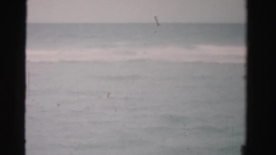 1955 Dade County home-movie frame showing pale ocean water, low surf lines, and dark vertical film borders.