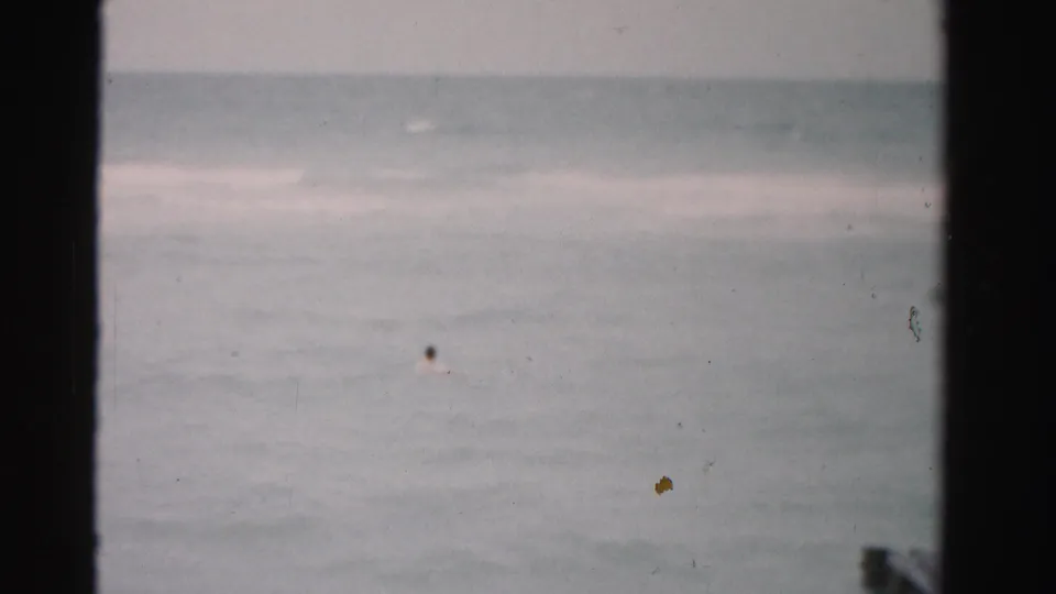 1955 Florida coastal home-movie frame showing open water, faint surf bands, soft focus, and visible film dust.