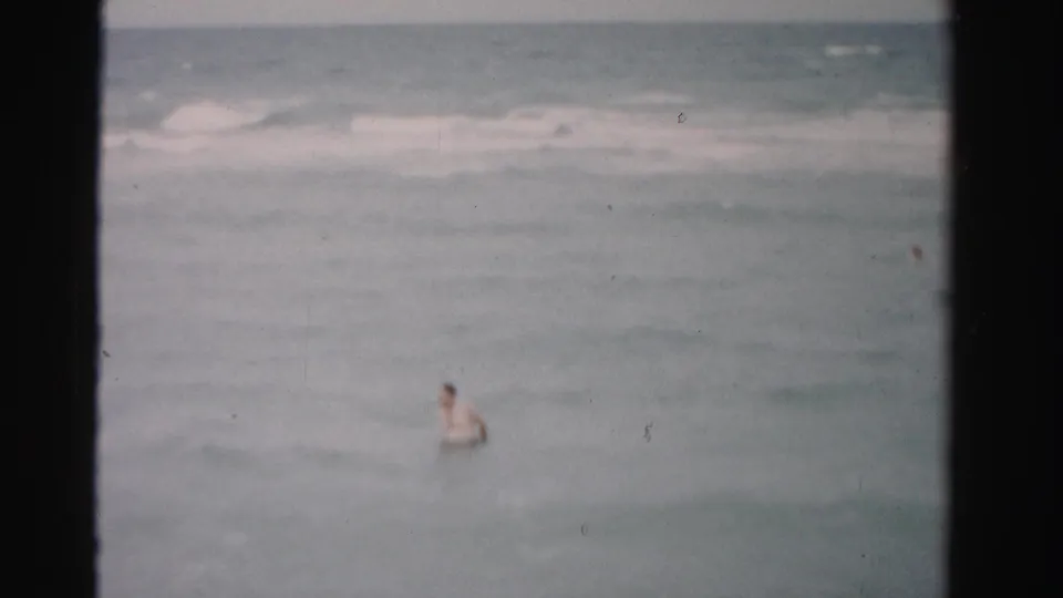 1955 Dade County beach footage shows a man in the ocean amid soft waves and faded 8mm color.