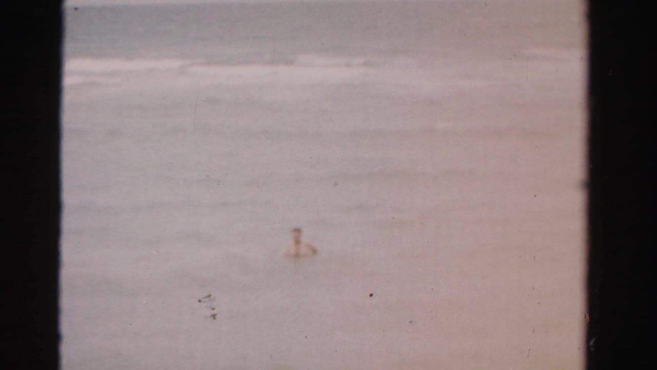 A distant swimmer is visible in hazy ocean water near rolling surf.
