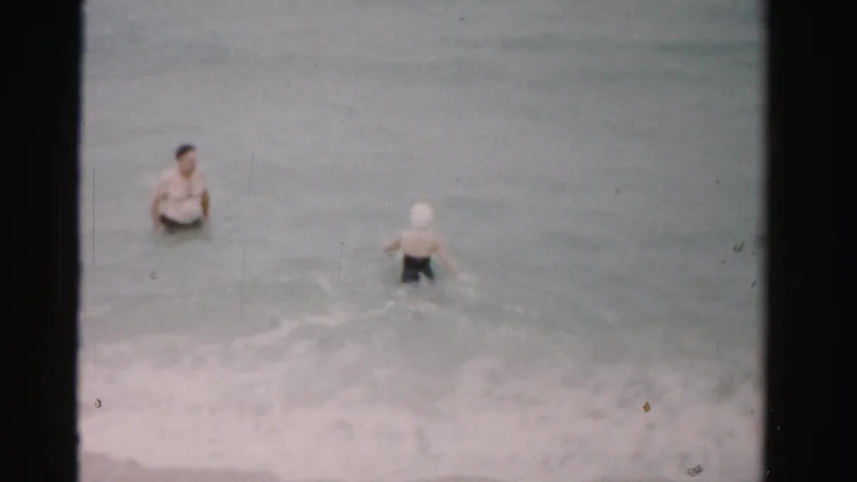 1955 Dade County 8mm frame showing the couple in waist-deep beach water, softened by grain and muted color.