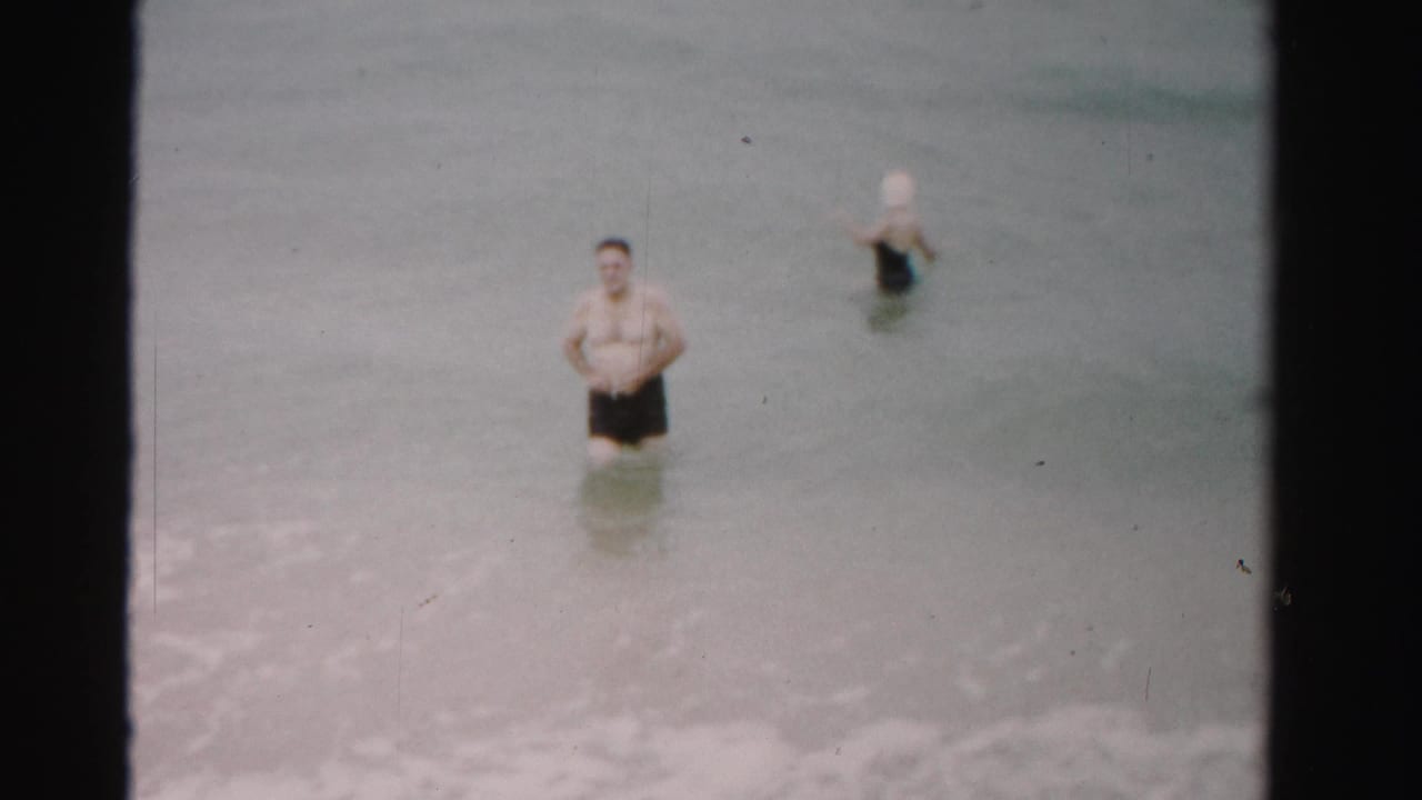 Man and woman wading in shallow ocean water near small waves.