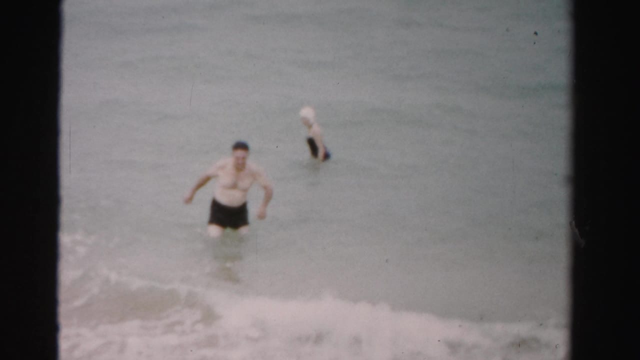 Man walking through surf with woman wading farther behind him.