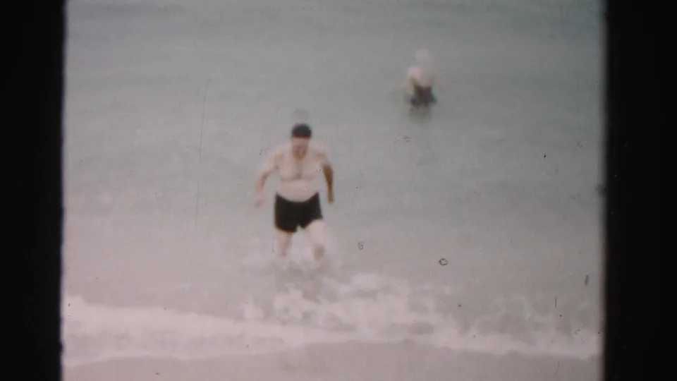 1955 Dade County ocean scene showing a man near shore with a woman blurred farther back in shallow water.