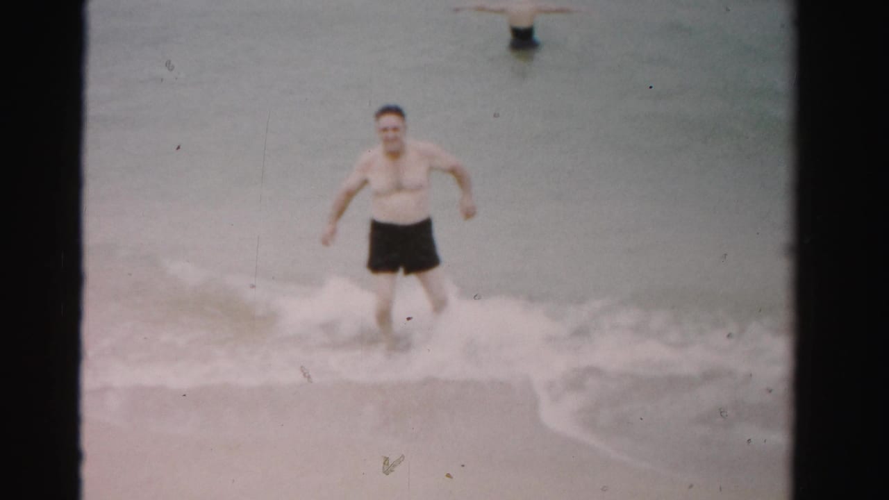 Man in dark swim trunks runs through shallow surf near the beach.