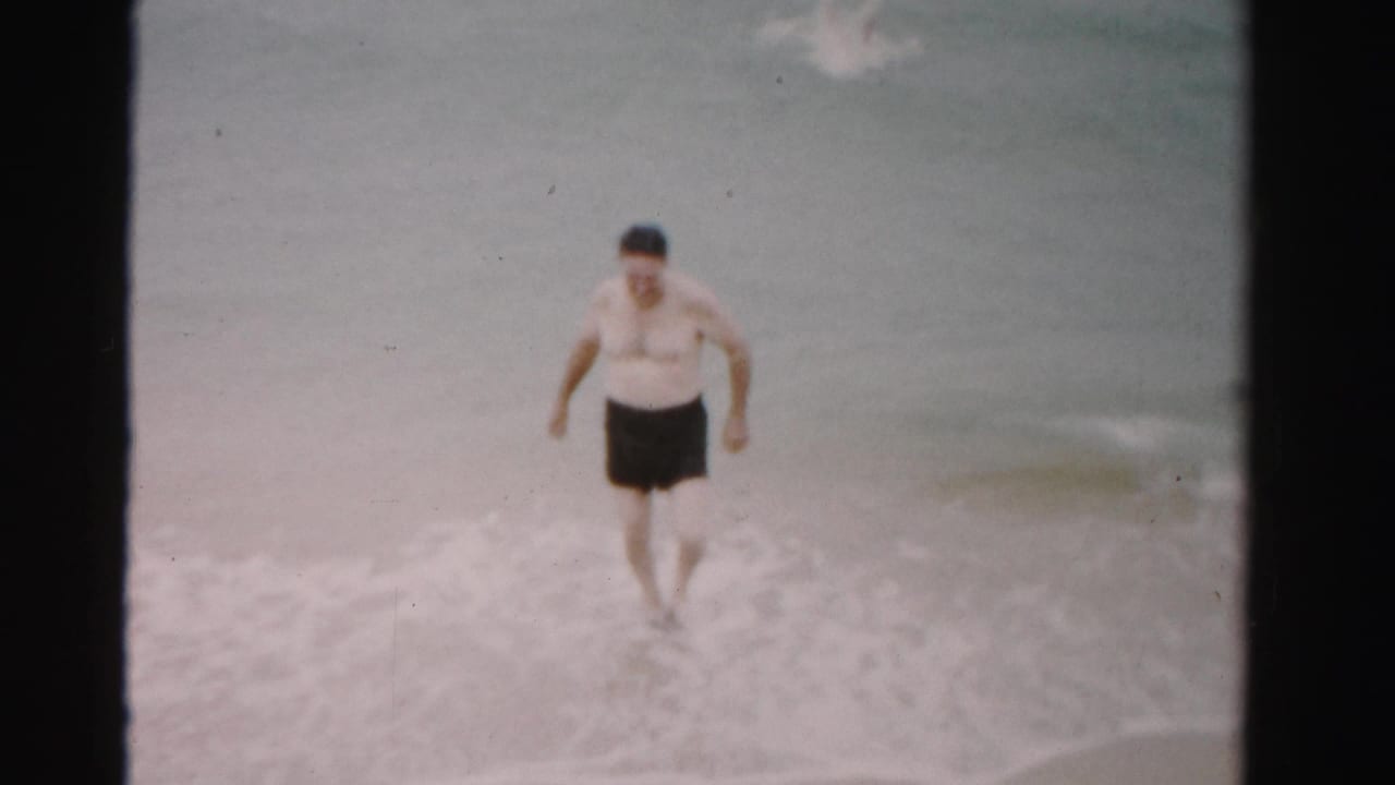Man walks out of foamy surf with ocean water behind him.