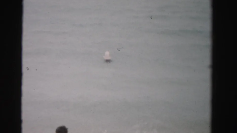 Open surf fills the frame, with a small distant swimmer or float visible in the water.