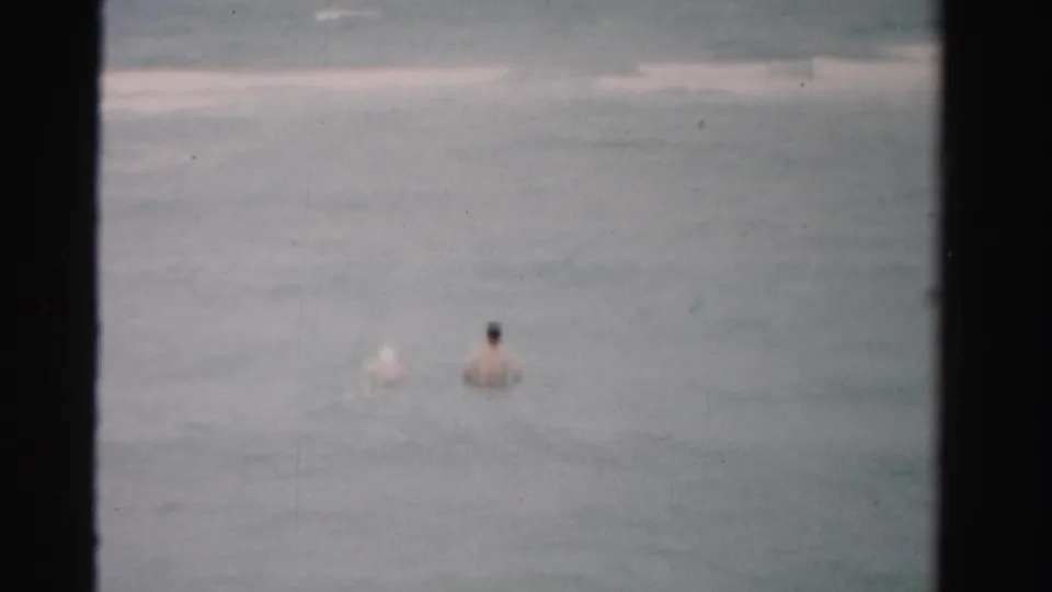 Distant swimmer wading in Dade County, Florida surf in 1955 8mm home-movie footage, with muted color and visible film wear.