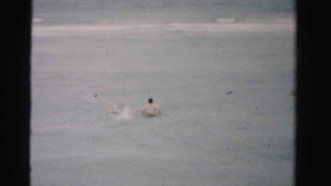 Swimmer seen from behind in ocean surf with a splash to one side.