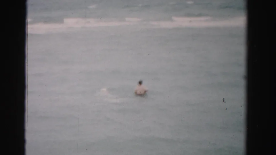 A lone swimmer remains partly surrounded by gentle Dade County, Florida waves in soft, grainy 1955 8mm footage.