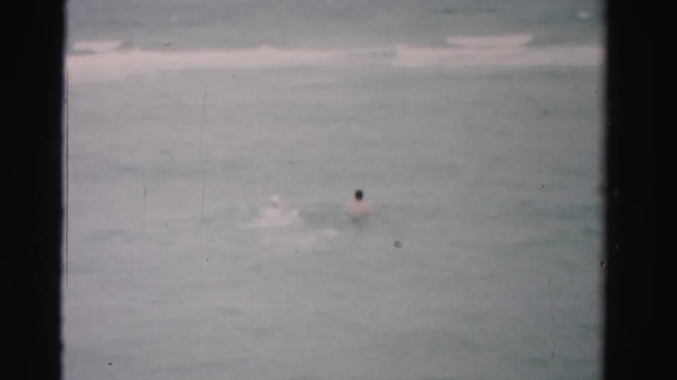 A distant swimmer in 1955 Dade County, Florida ocean water appears beside a small splash in grainy 8mm home-movie footage.