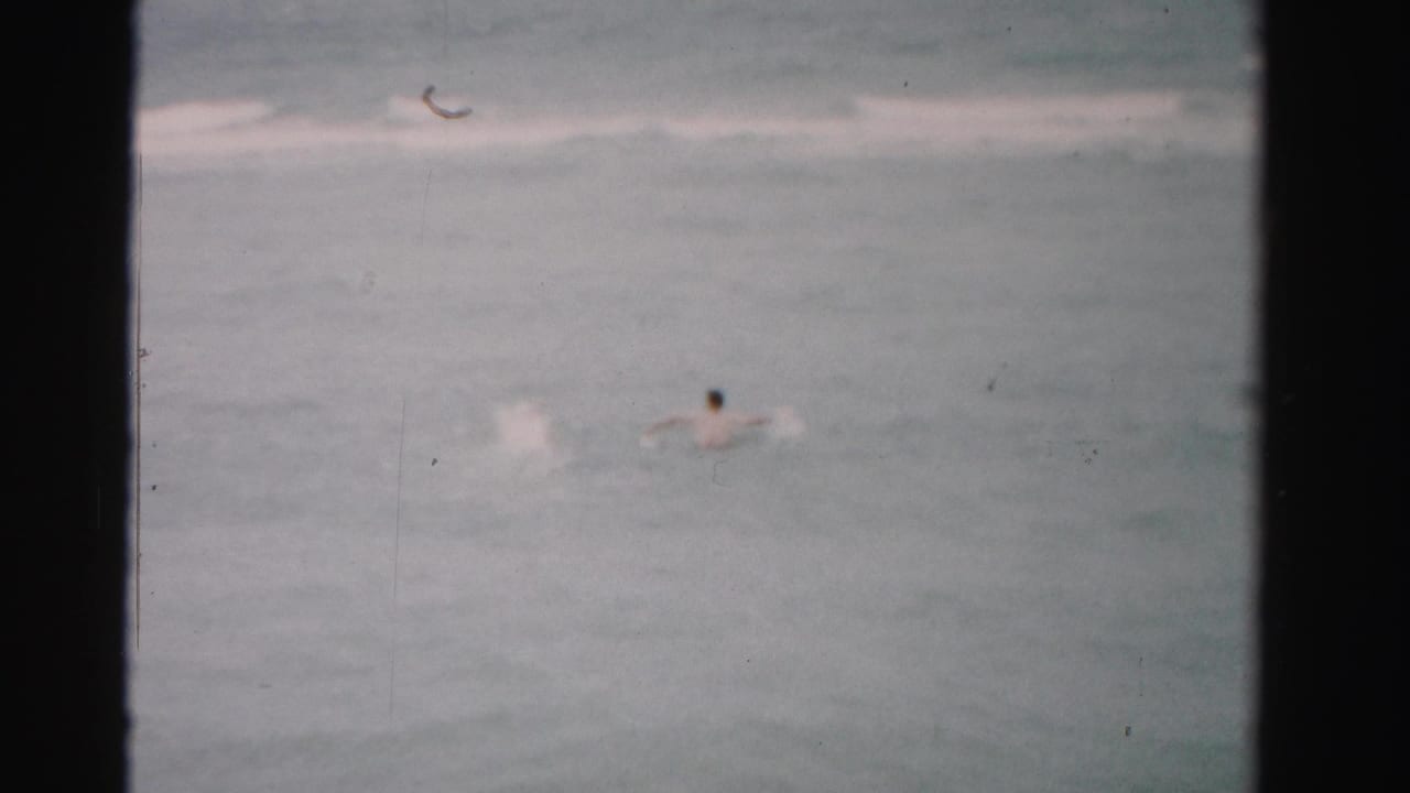 Dade County, Florida ocean scene with distant swimmers, pale wave lines, and visible 8mm film gate borders.