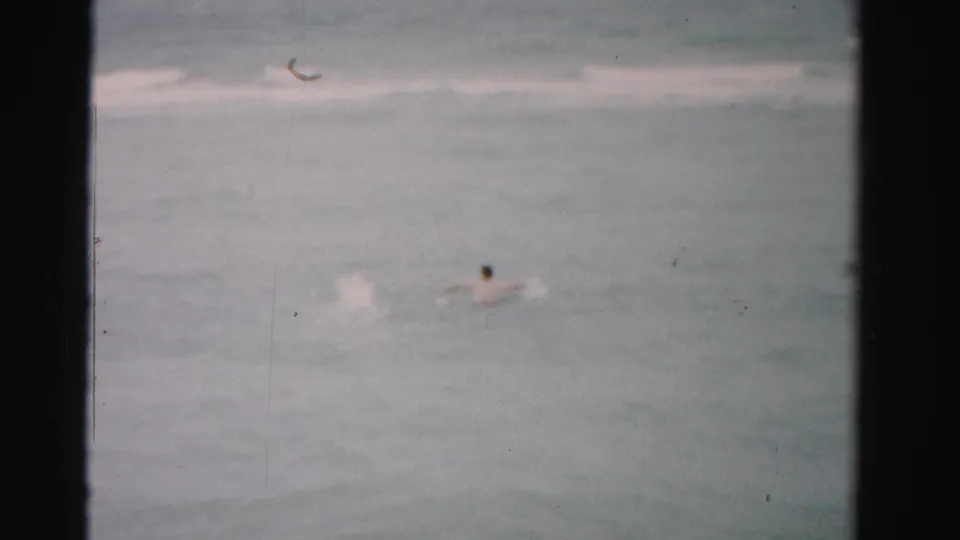 Dade County, Florida ocean scene with distant swimmers, pale wave lines, and visible 8mm film gate borders.