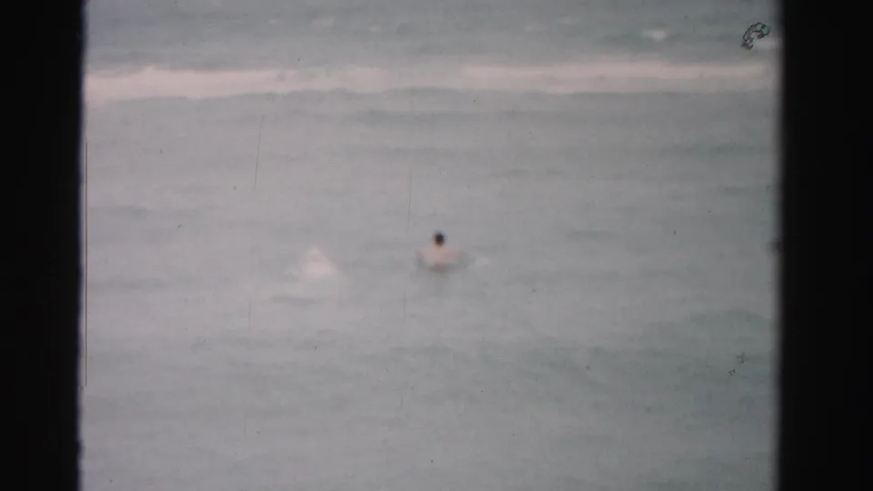 1955 home-movie still of a swimmer in Dade County surf, with another splash visible nearby and strong film-frame edges.