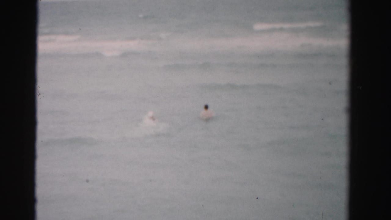 Two distant swimmers in the ocean beneath an overcast sky.