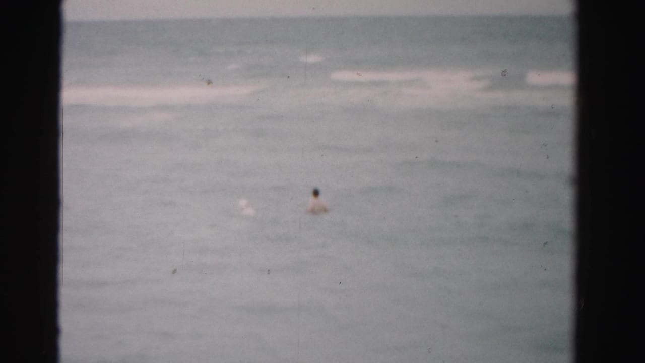 Dade County 1955 home-movie still showing distant swimmers in the ocean, with soft focus and visible film texture.