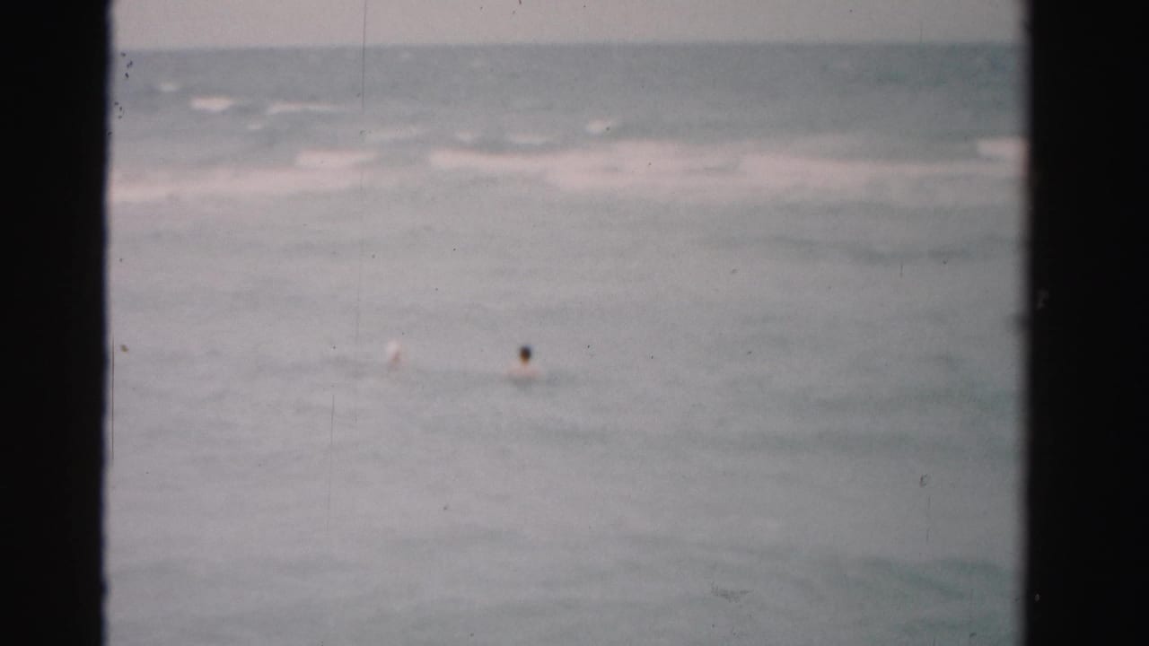 Distant swimmer floating in open ocean under a pale horizon.