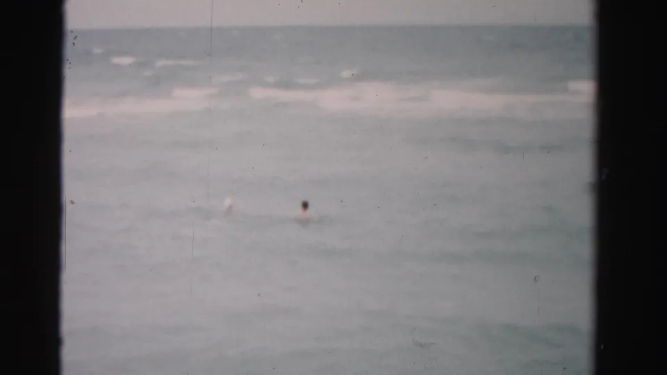 1955 Dade County 8mm frame with a distant swimmer in calm ocean water beneath an overcast horizon.