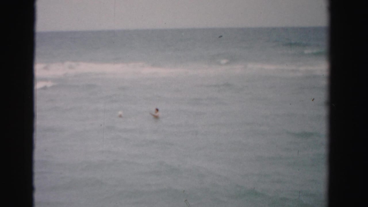 Two distant swimmers appear in calm ocean water near a soft surf line.