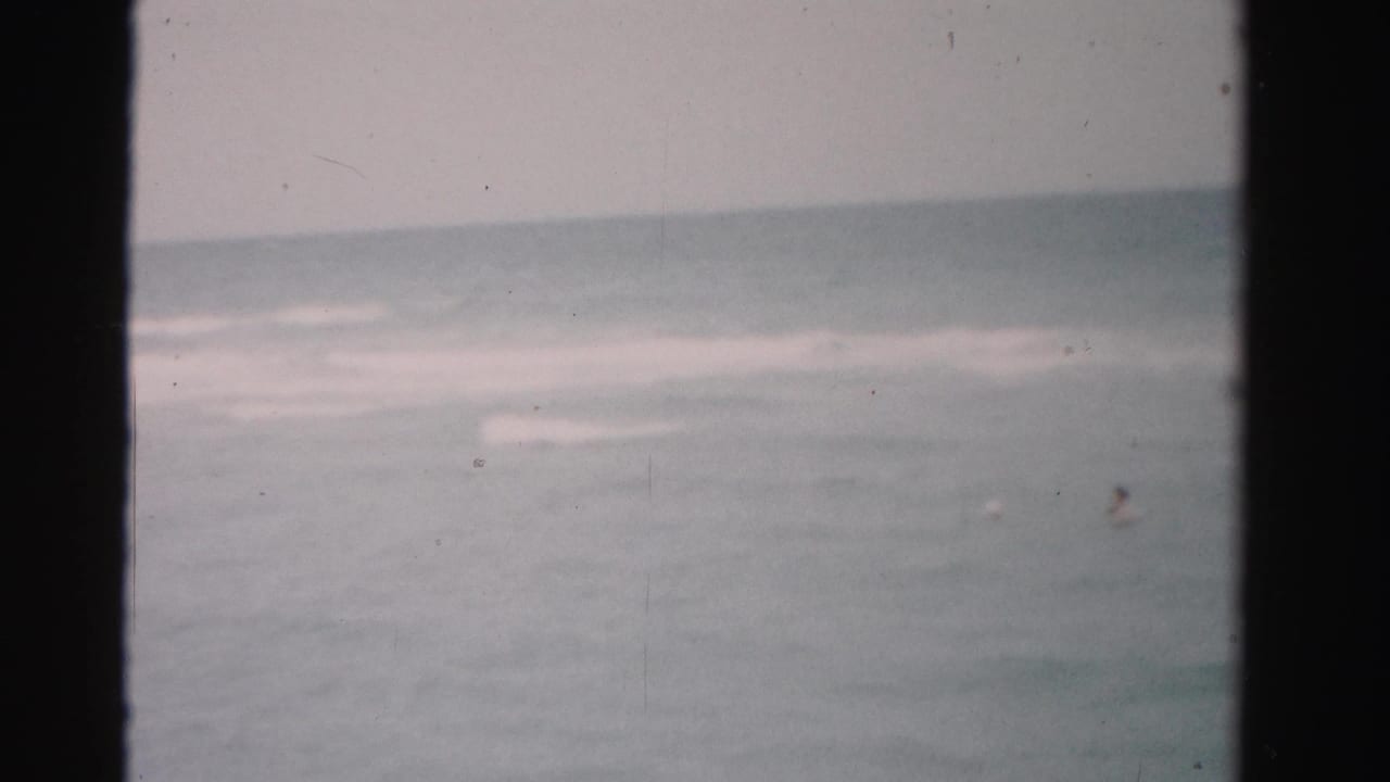 Dade County 8mm beach frame with soft waves and a small distant swimmer partly visible in the ocean.