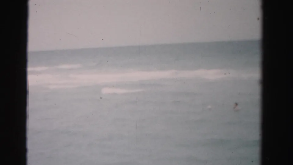 Dade County 8mm beach frame with soft waves and a small distant swimmer partly visible in the ocean.
