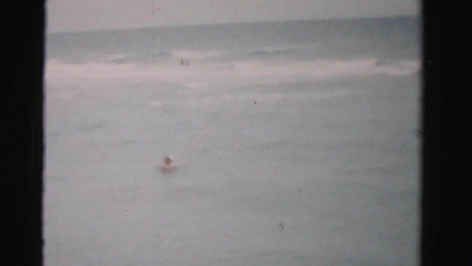 1955 Florida home-movie frame with a distant swimmer in open water and muted surf near the horizon.