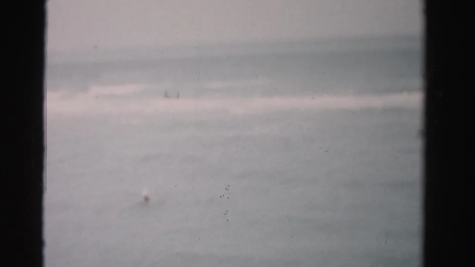 Soft 8mm view of the Dade County sea, with a tiny swimmer visible low in the frame beneath distant surf.