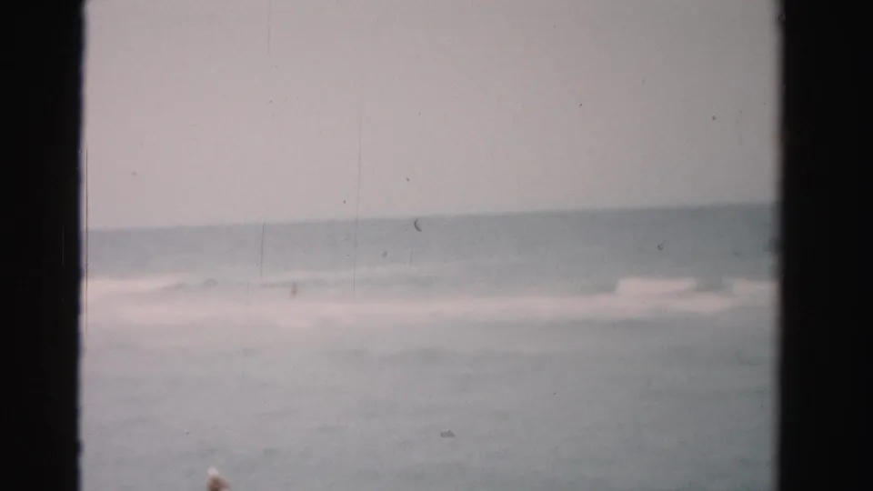 1955 Dade County beach footage frame with a faint swimmer near the lower edge and broad gray-blue water beyond.