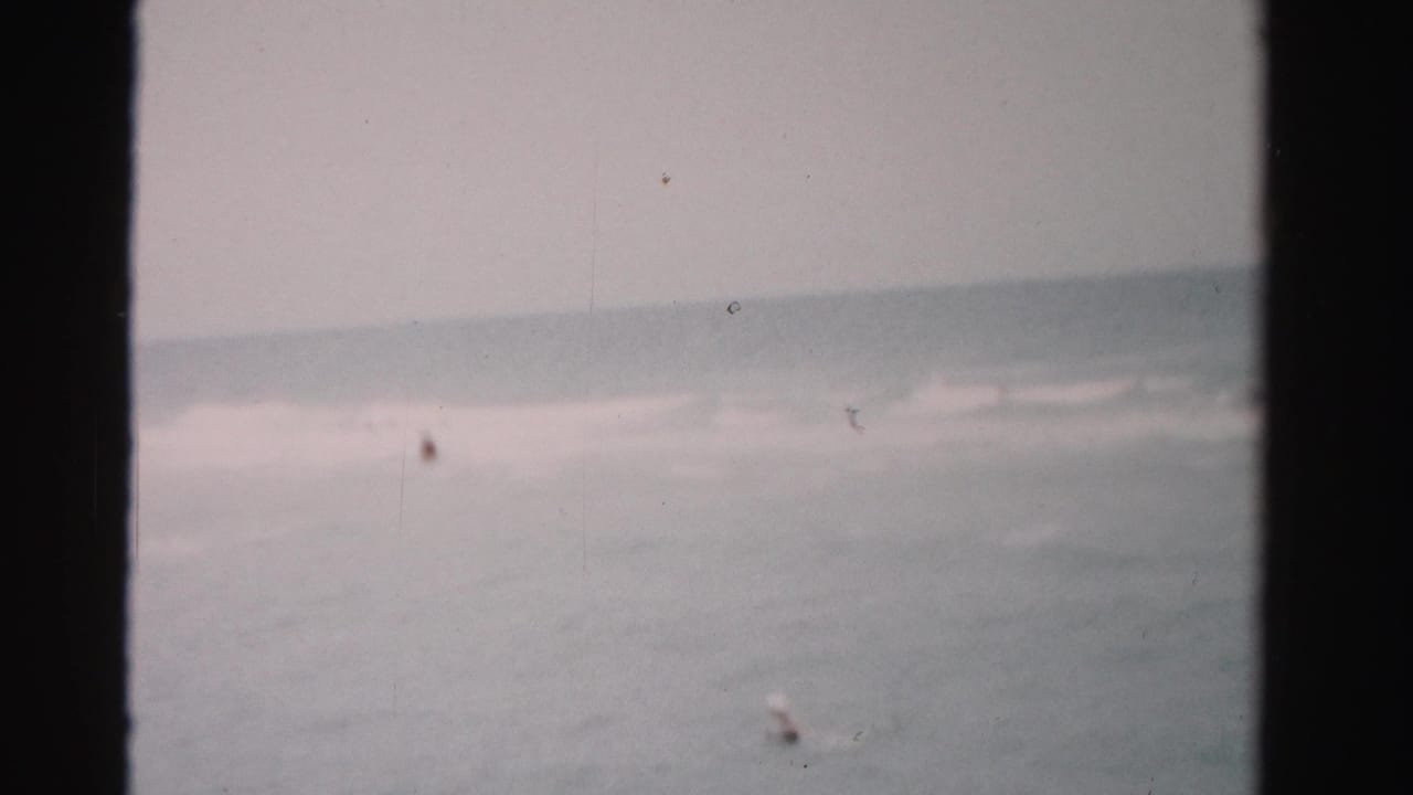 Ocean waves with tiny distant swimmers near the right side of the frame.