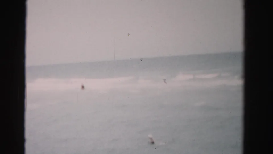 1955 Dade County ocean view with small distant swimmers in the surf beneath an overcast sky.