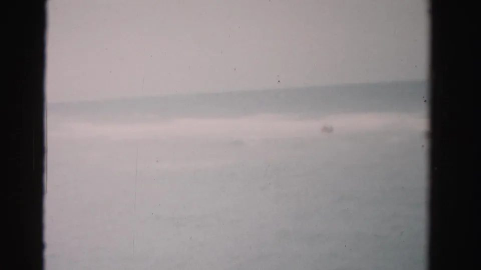 1955 Dade County ocean frame showing faint distant swimmers or splashes beyond gentle waves.